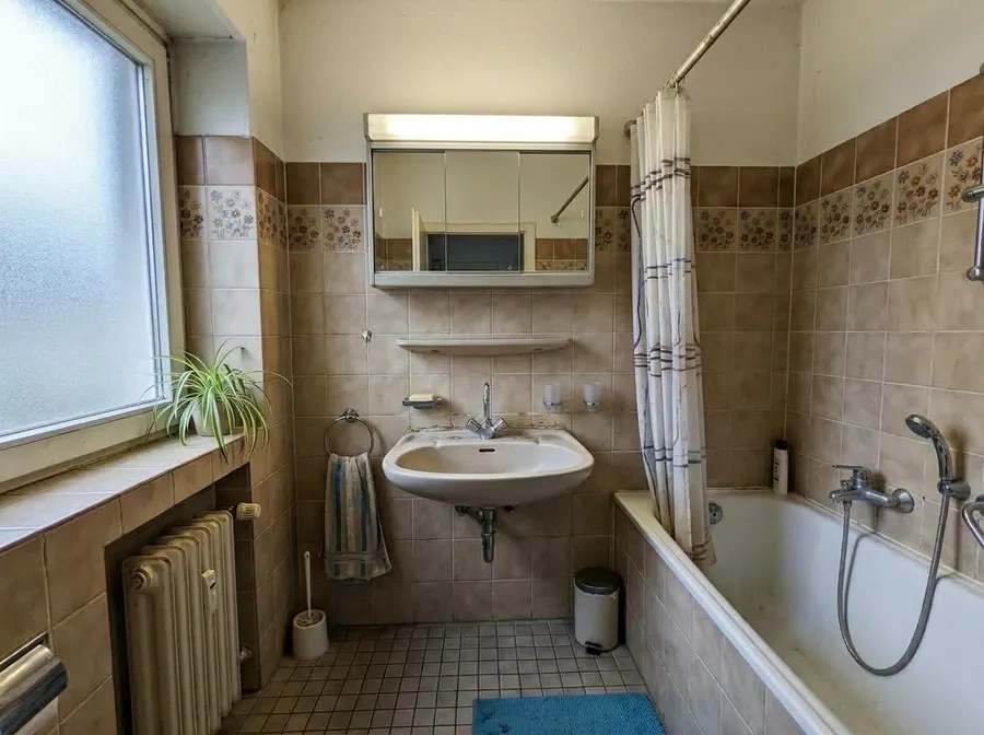 Vorher: Badezimmer aus den 80er Jahren mit beigen Fliesen, Blumenbordüre und Badewanne (Symbolbild)
